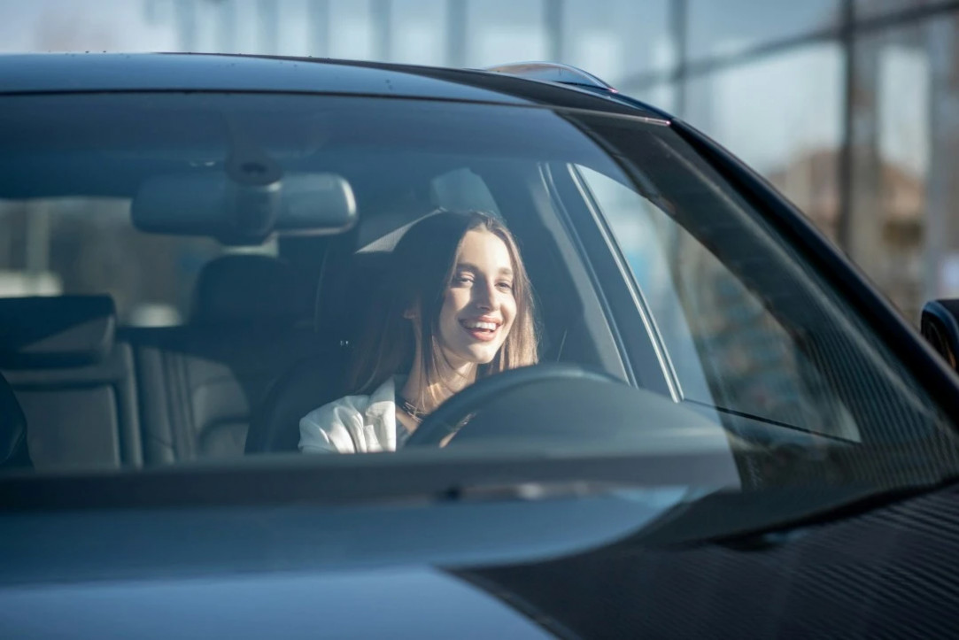 a smiling woman is seated in the driver's seat of a modern vehicle