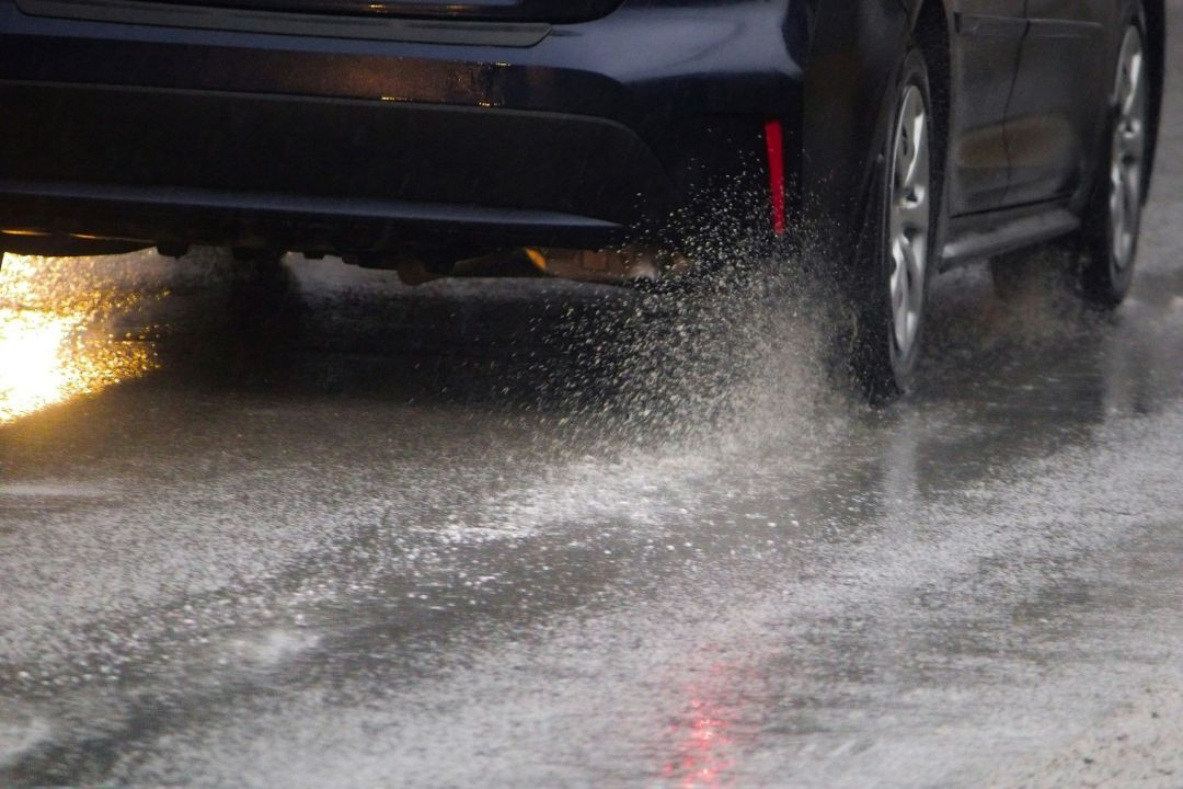 car driving through standing water on a rain-soaked road