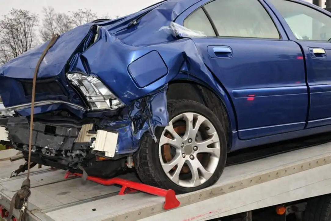 severely damaged rear end of a blue sedan loaded on a tow truck after a crash