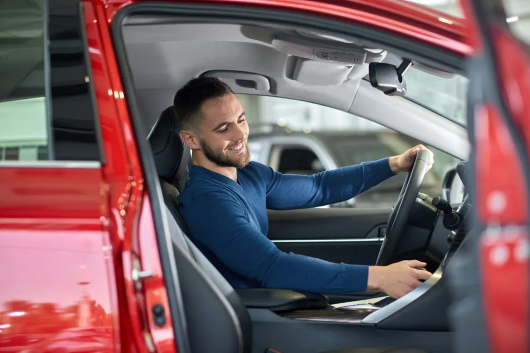 man sitting in the driver's seat of a red car, adjusting controls and preparing for a test drive