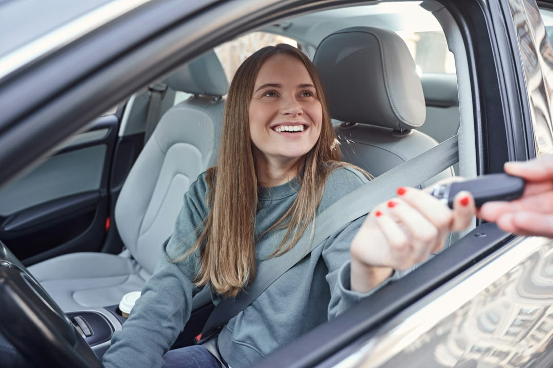 smiling young woman sitting in a car and receiving the car keys